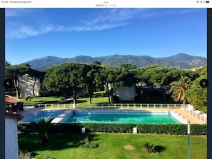 Ein Schwimmbecken, umgeben von gepflegtem Rasen und Bäumen, mit Bergen im Hintergrund.