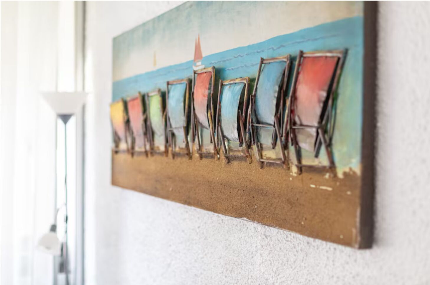 Une œuvre d’art murale représentant une rangée de chaises colorées sur fond de plage.