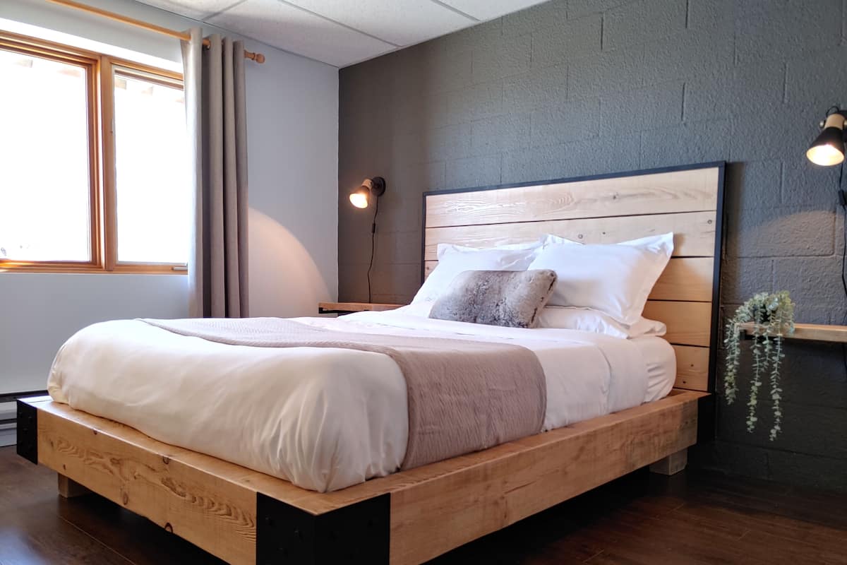 A modern bedroom with a wooden bed frame, a headboard, and a bedside lamp.