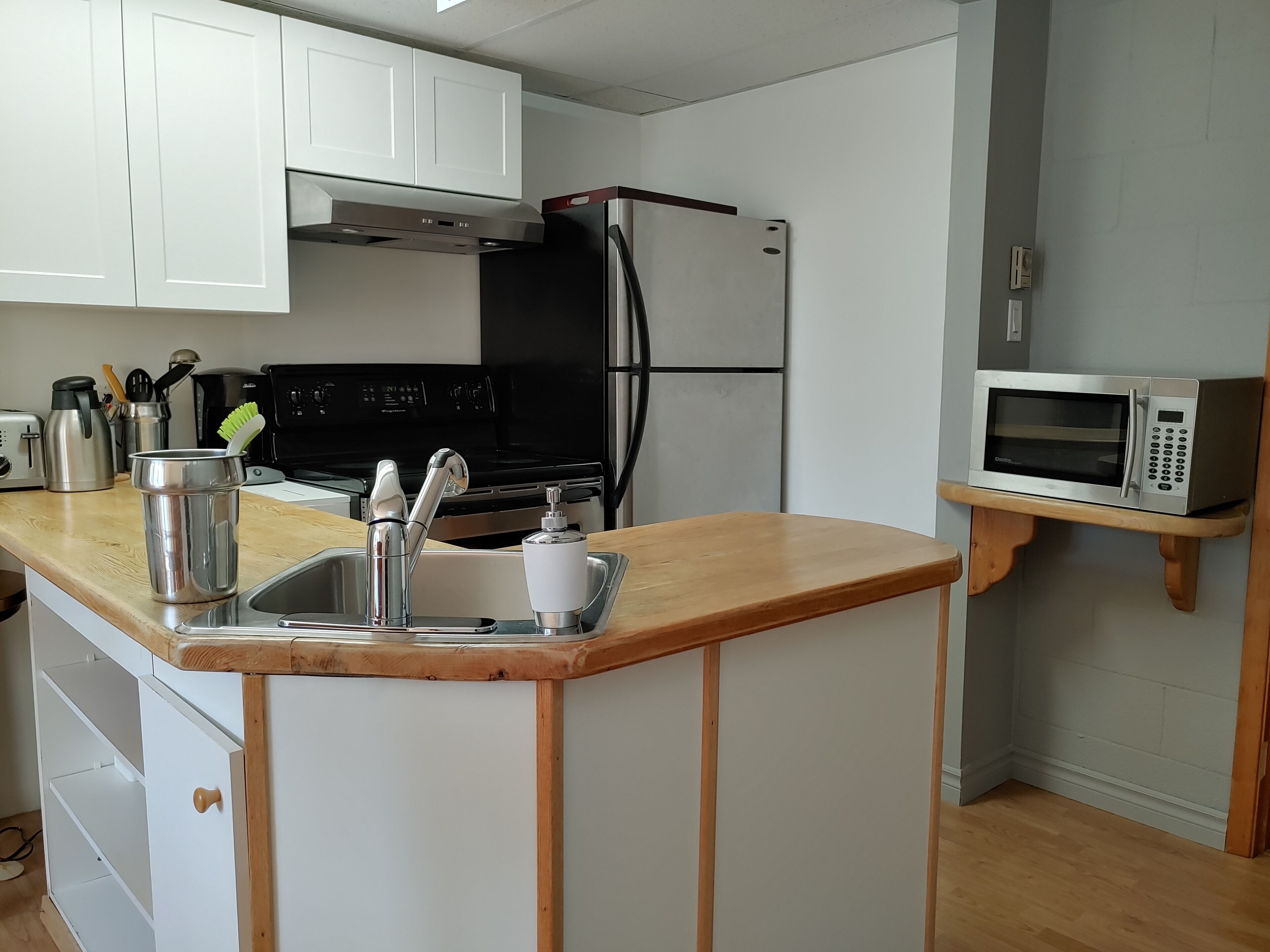Cocina compacta con armarios blancos, pileta de acero inoxidable, microondas y heladera negra.