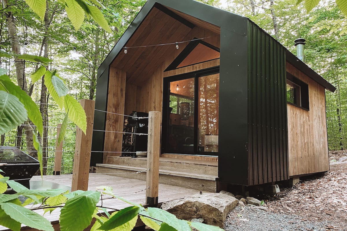 A small wooden cabin with a porch, surrounded by trees.