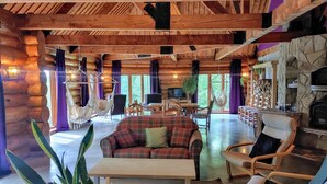 A log cabin interior with a central seating area, a stone fireplace, and a television.