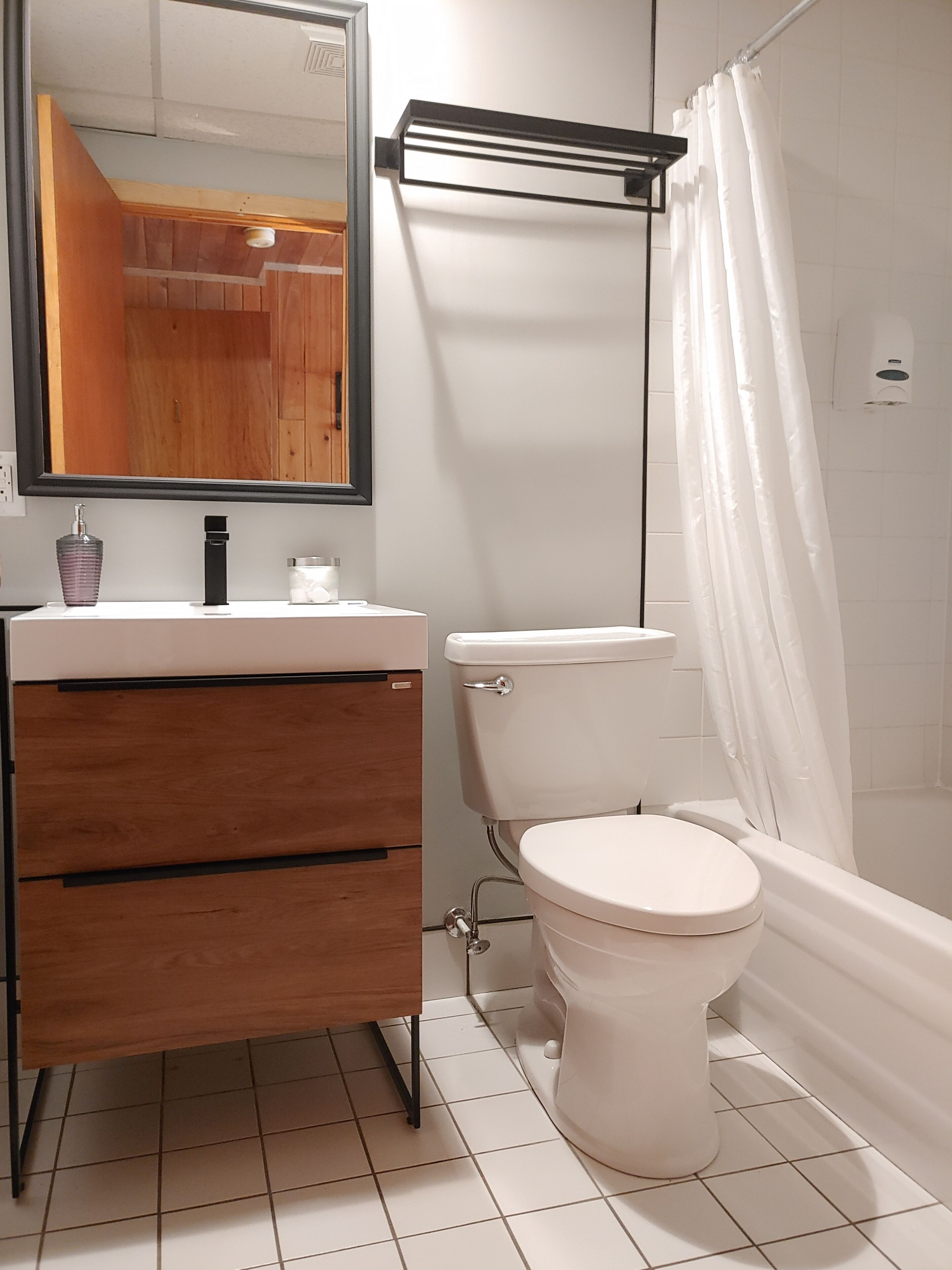A bathroom with a white toilet, a wooden vanity, a mirror, and a shower curtain.