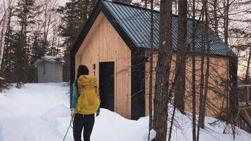 A person with a yellow backpack pulling a sled with a black container filled with clothes.
