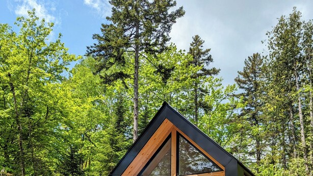 A wooden cabin with a deck, large windows, and a grill area.