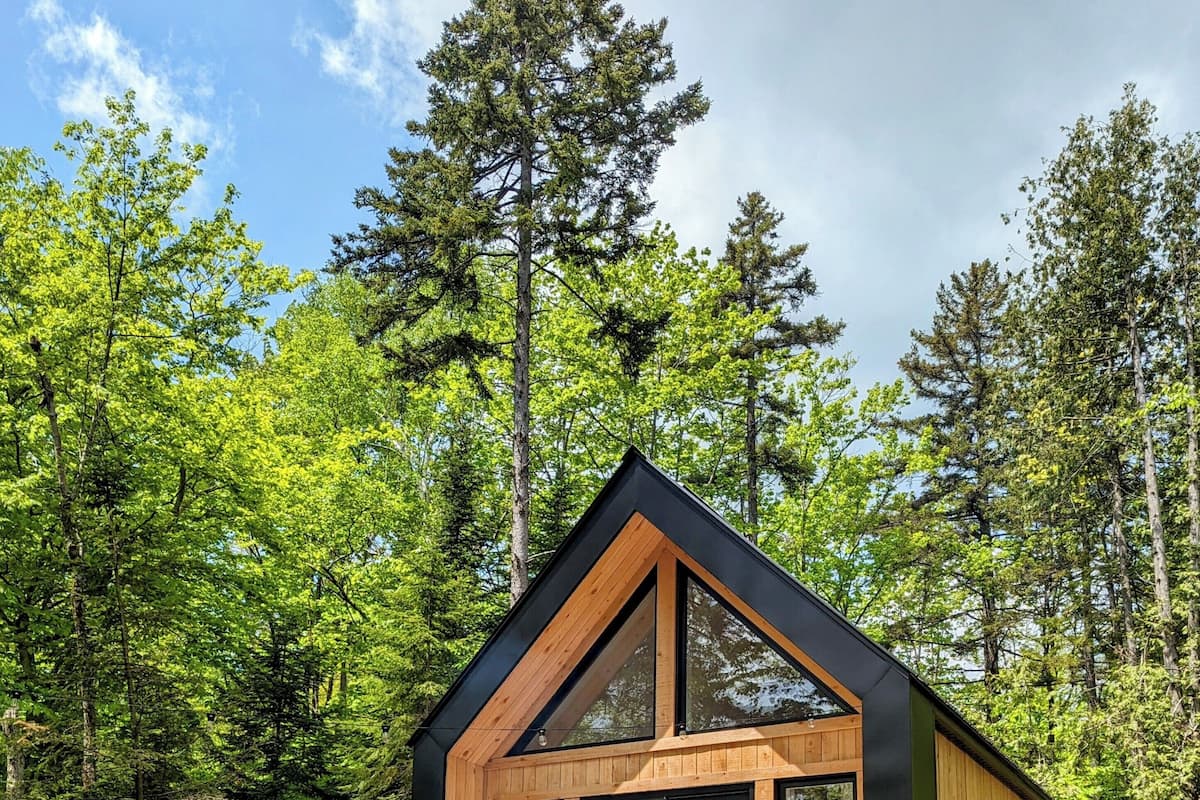 A wooden cabin with a deck, large windows, and a grill area.