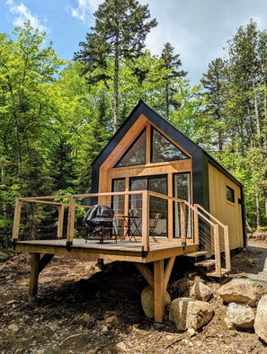 Una cabaña de madera con terraza, ventanas amplias y zona de barbacoa.