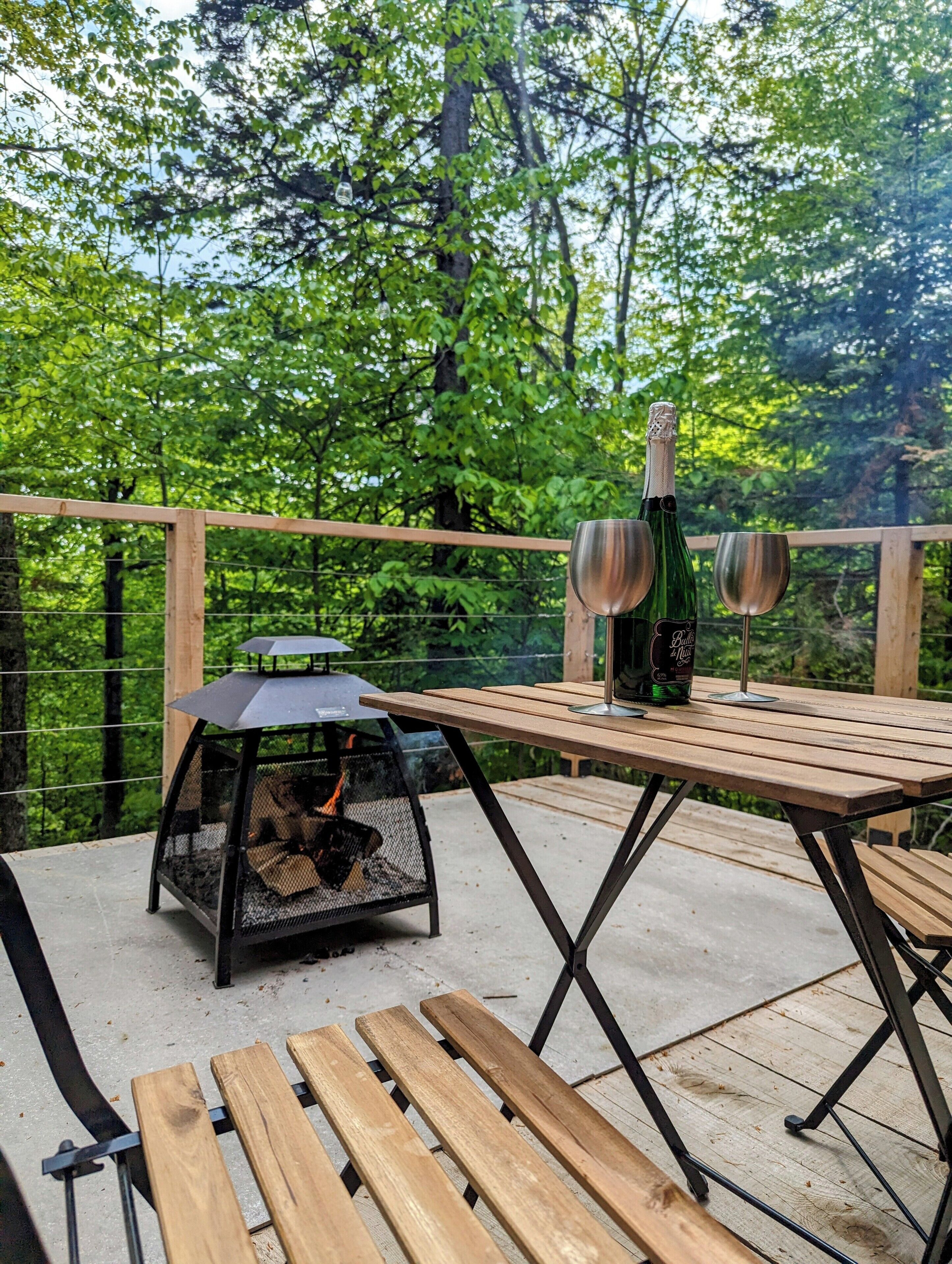 A wooden deck with a table, two wine glasses, and a bottle of wine.