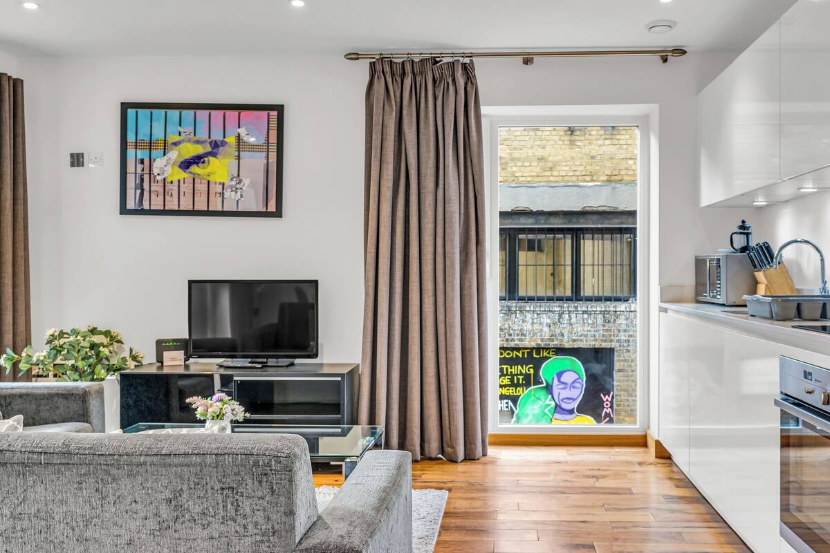 A modern living room with a flat-screen TV, grey sofas, a coffee table, and a painting on the wall.