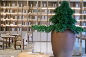 Un intérieur moderne agrémenté d’un grand arbre en pot, de chaises en bois et d’un mur à motifs.