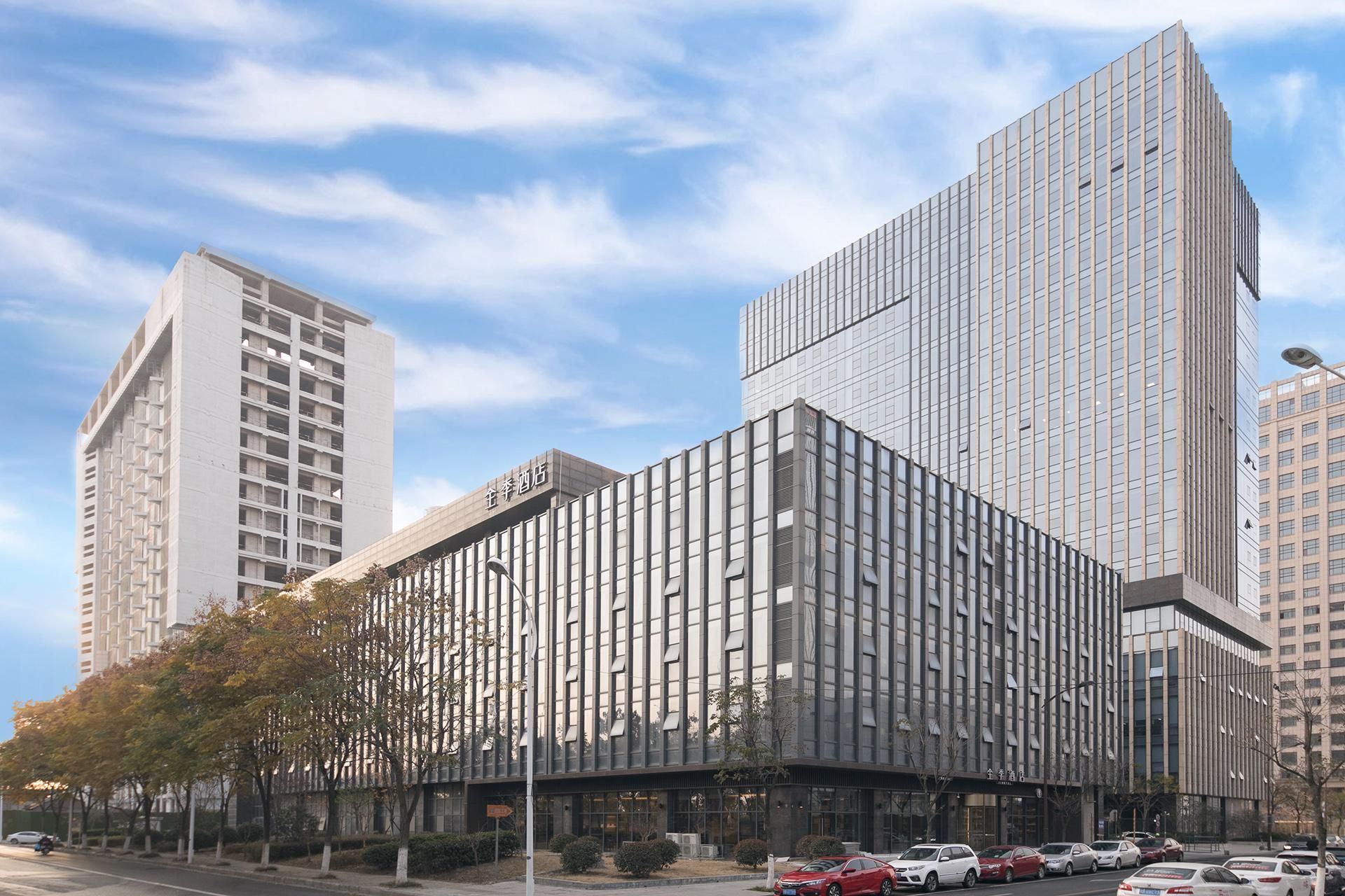 A modern hotel with a prominent vertical facade, large windows, and a parking lot with several cars.