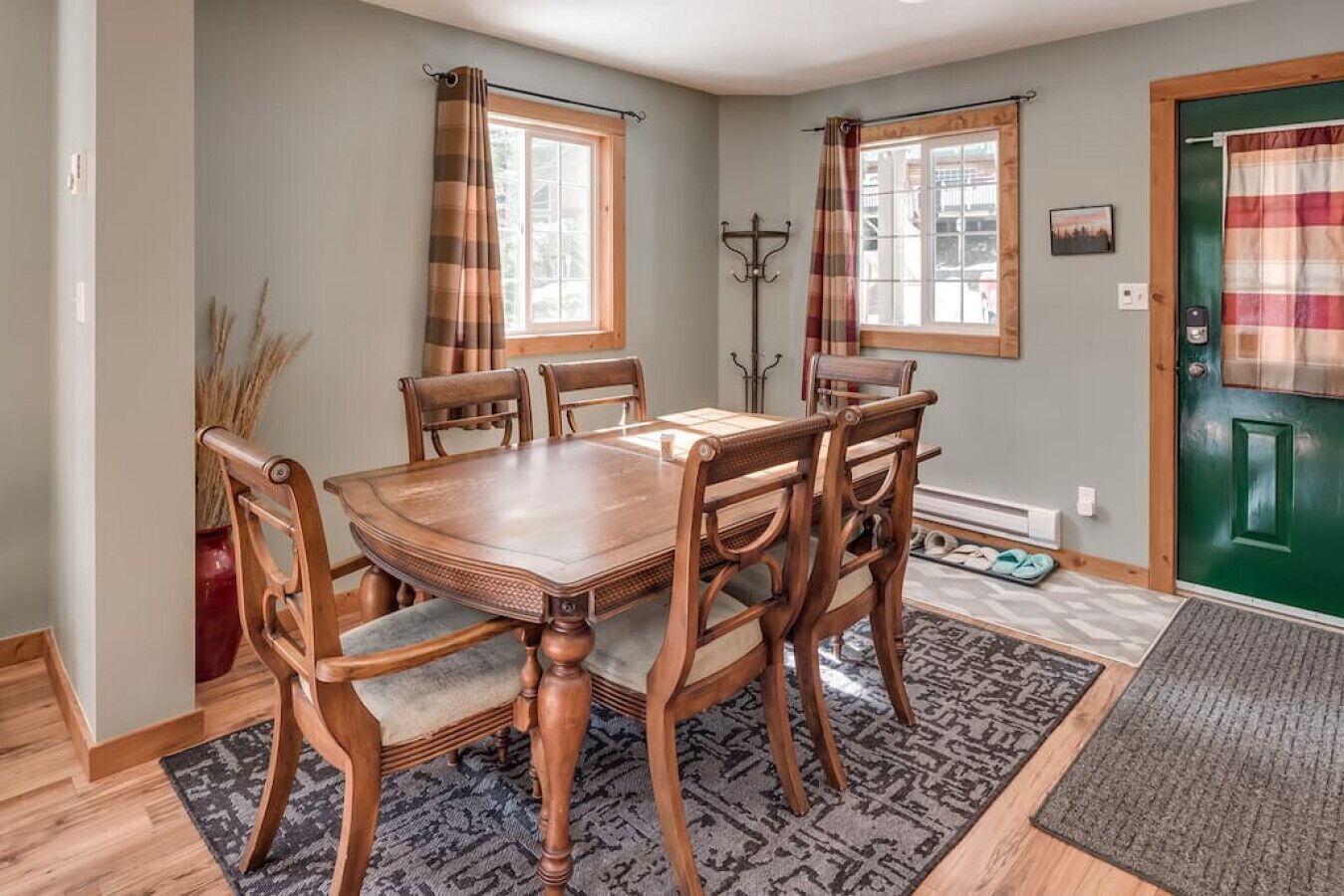 Un coin repas avec une table et des chaises en bois, un tapis à motifs et une porte verte.