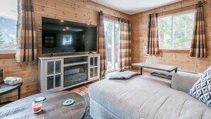 A cozy room with a large flat-screen TV on a wooden cabinet, a sofa, a small table with a candle, and a window with curtains.
