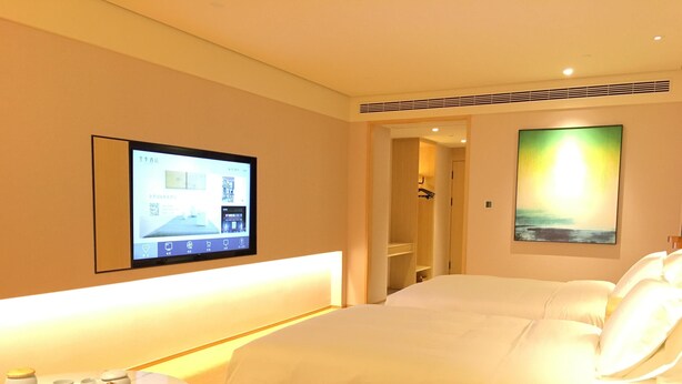 Una habitación de hotel con una cama, un televisor montado en la pared, un cuadro y una mesita con tetera y tazas.
