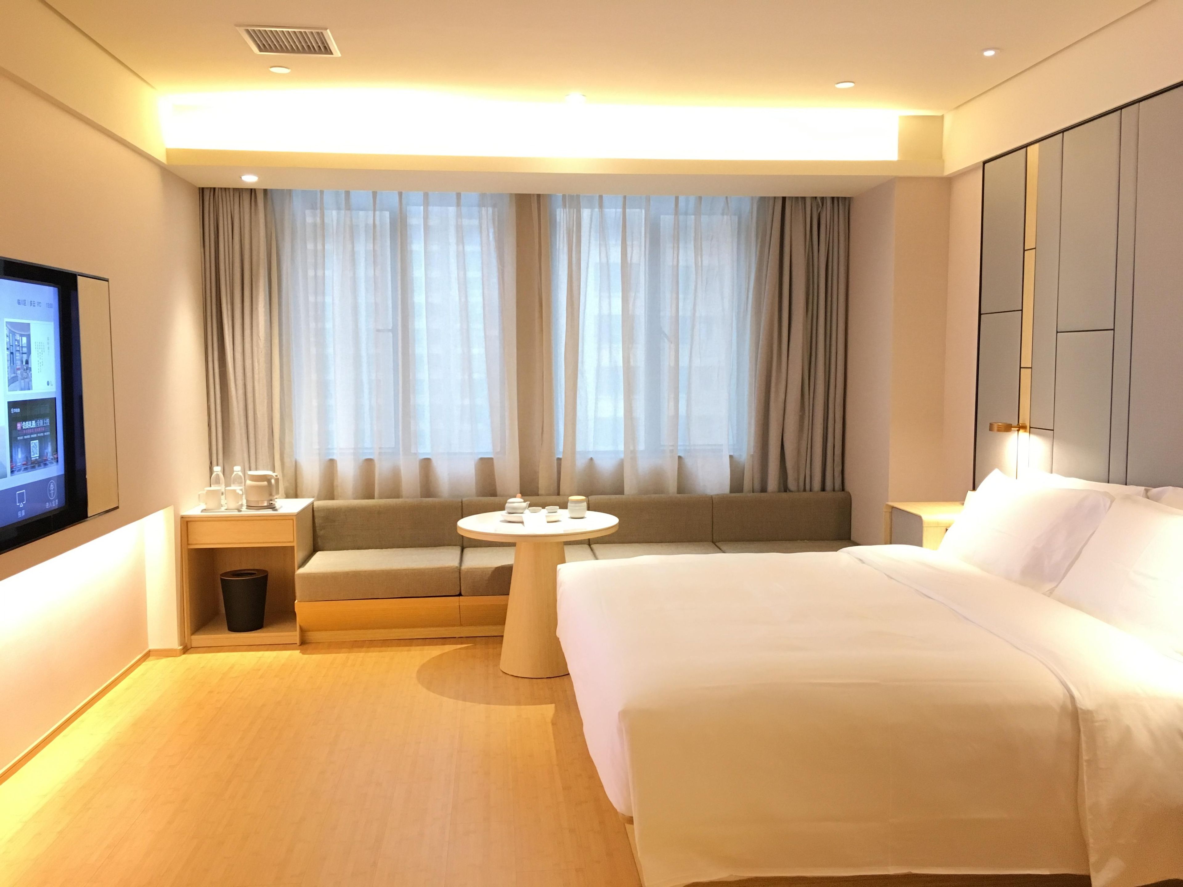 A hotel room with a bed, a sofa, a small table, a TV, and a window with curtains.