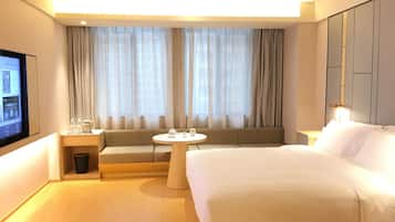A hotel room with a bed, a sofa, a small table, a TV, and a window with curtains.