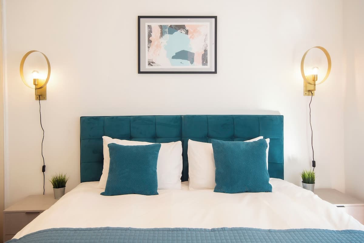 A neatly made bed with teal and white bedding, a teal headboard, and two wall-mounted light fixtures on either side.