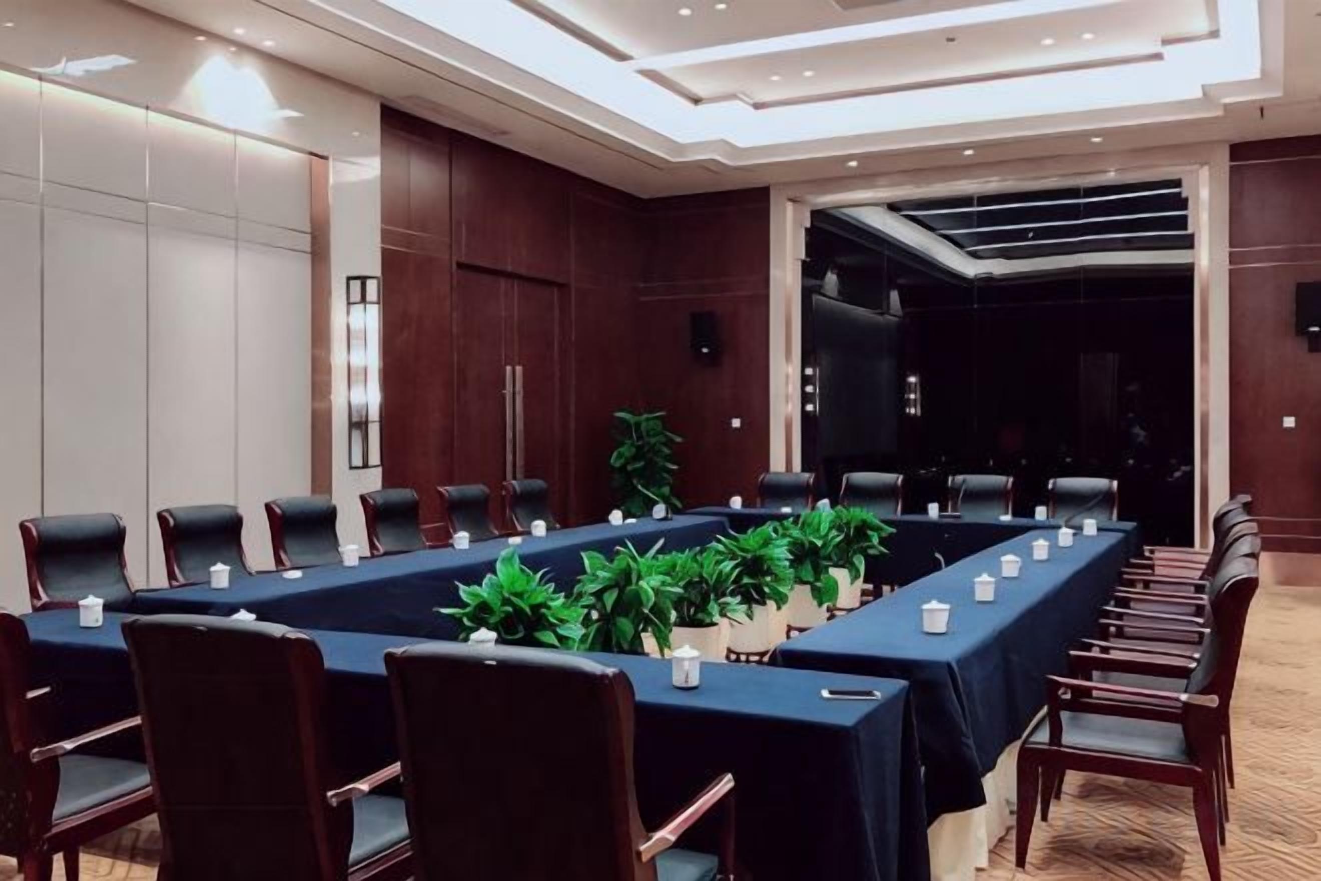 Una sala conferenze con un lungo tavolo, sedie e piante in vaso.