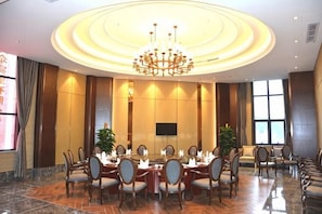 A conference room with a round table, chairs, a chandelier, and a large screen.