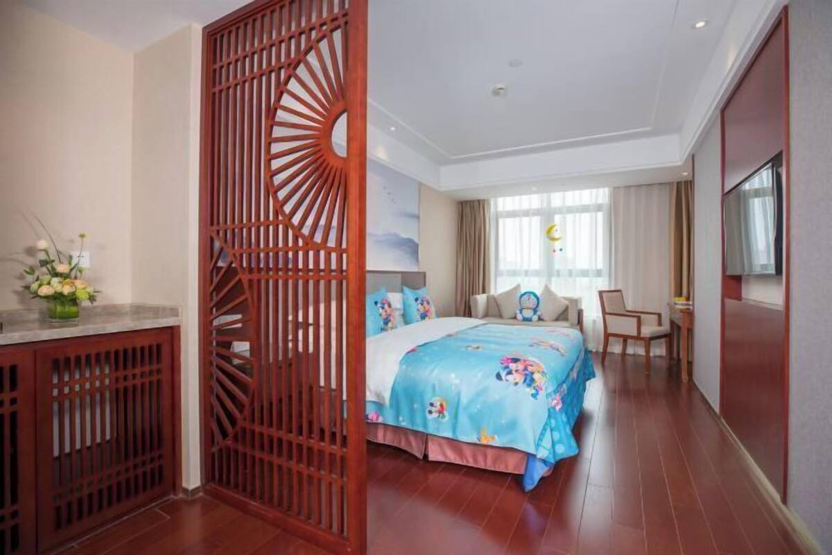 A hotel room with a bed, a desk, a chair, and a decorative wooden partition.