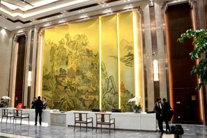 Un hall d’hôtel comprenant une grande fresque murale, un comptoir d’accueil, un espace salon et une porte.