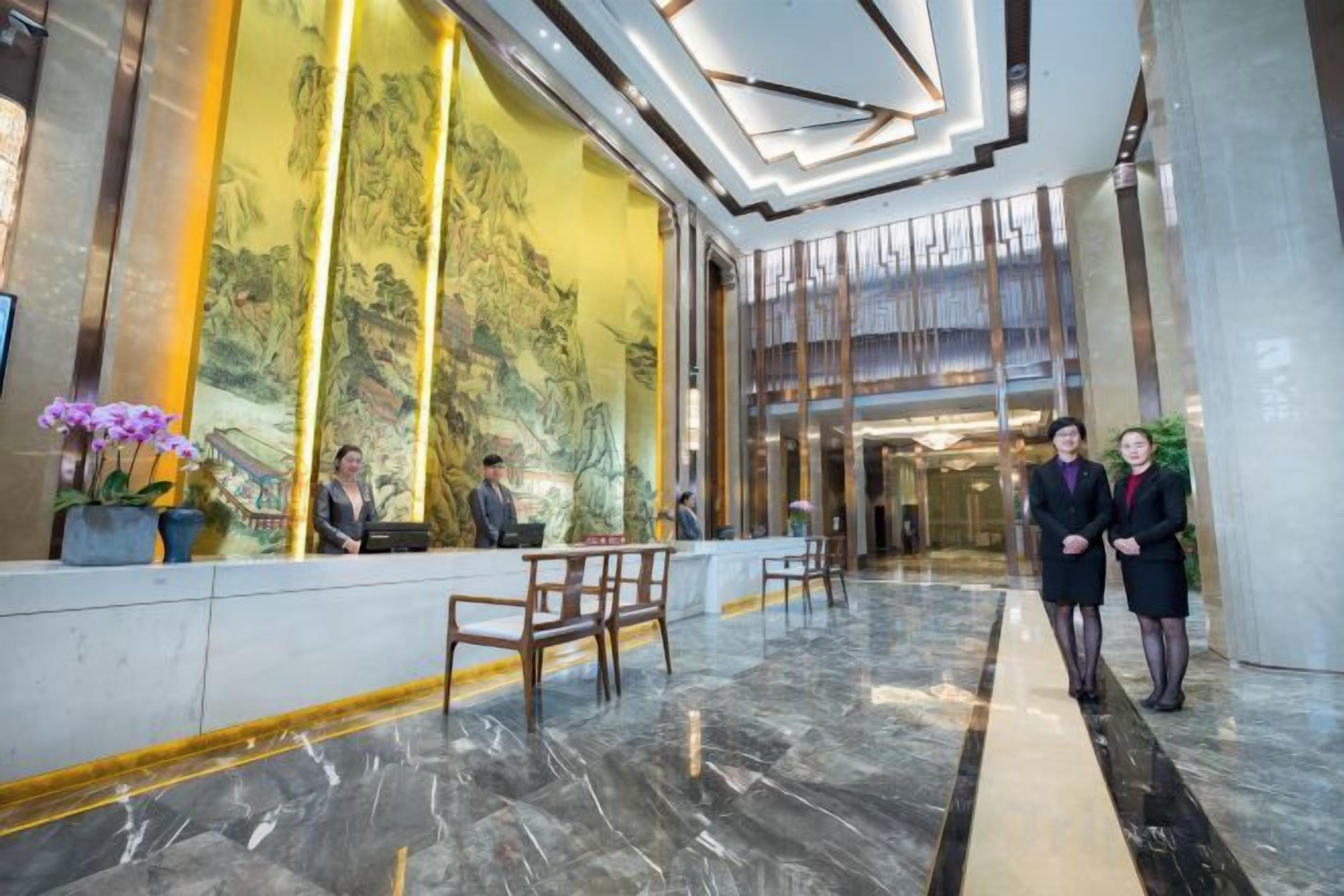 A hotel lobby with a reception desk, seating area, and a large mural.