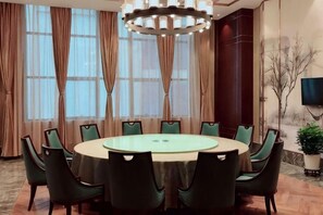A conference room with a round table, chairs, a chandelier, large windows with curtains, and a television. - Lanxin Hotel (Shaoxing)