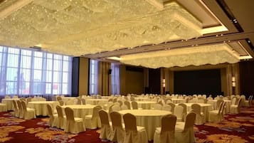 A banquet hall with round tables and chairs, large windows, and a decorative ceiling.