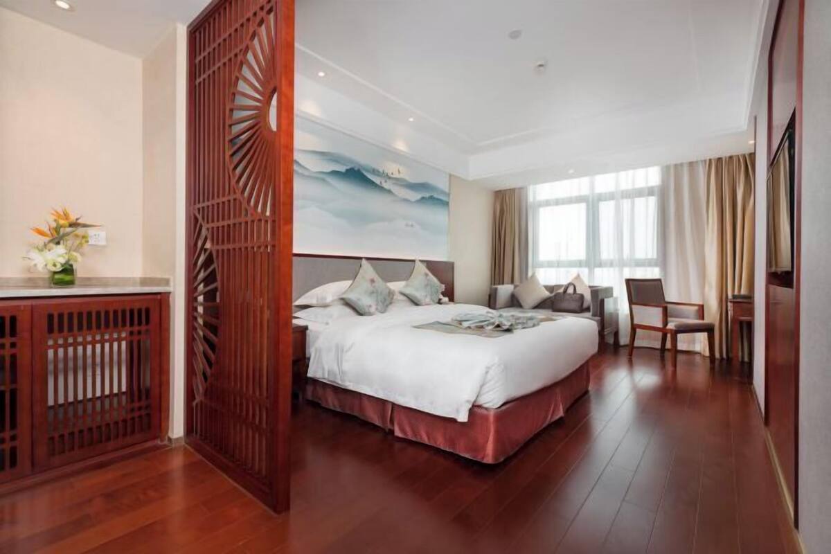 A hotel room with a large bed, a desk, and a view of a mountainous landscape through the window.