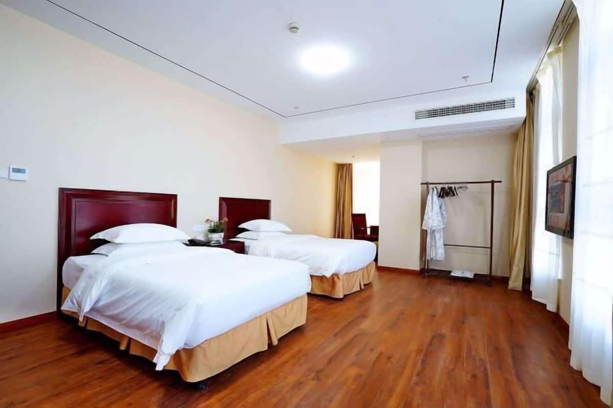 A hotel room with two beds, wooden flooring, a wardrobe, and a shower area.