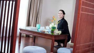 A room with a wooden table set with a vase of flowers, a teapot, and cups. There are cushions on the floor and a wooden partition in the background.
