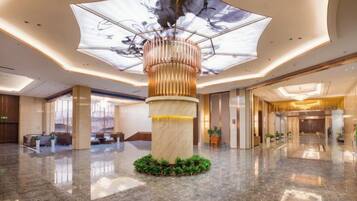 A spacious lobby with a central column, a ceiling artwork, and a reception desk.