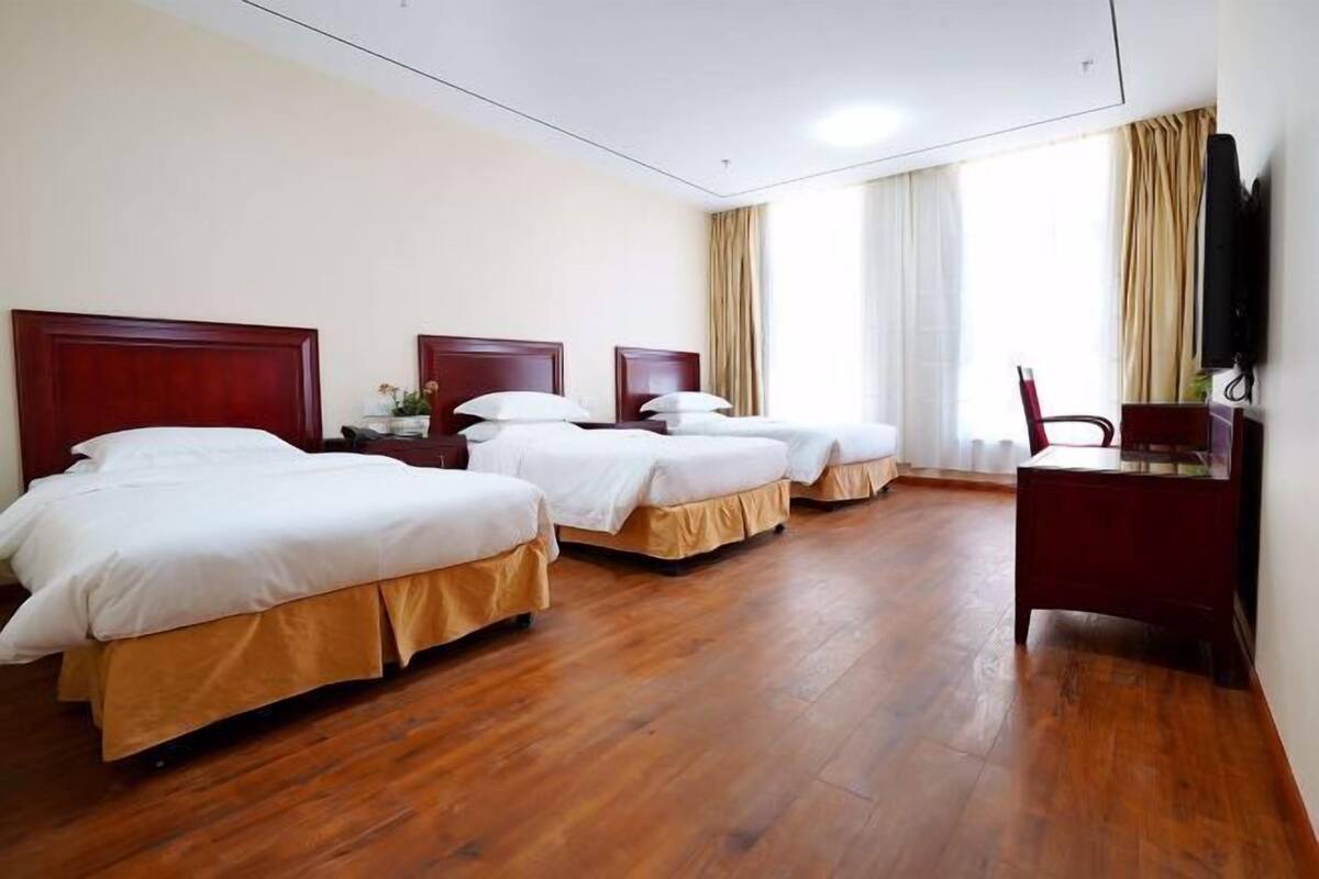 A hotel room with three beds, wooden flooring, a desk, and a television.