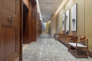 A hallway with wooden paneling, a marble floor, and a reception desk with chairs. - Lanxin Hotel (Shaoxing)