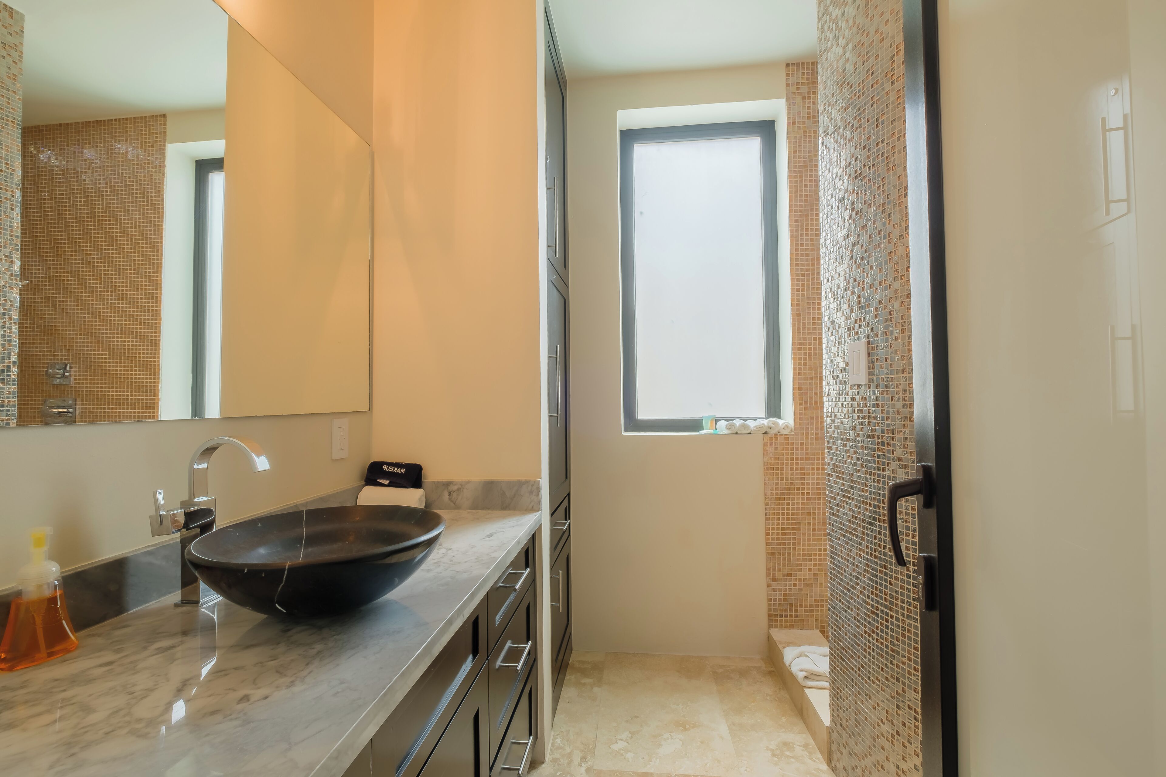 A modern bathroom with a large mirror, a black vessel sink, and a window.