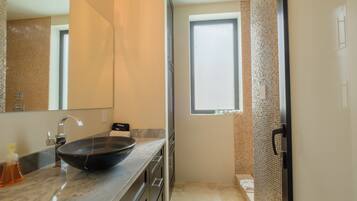 A modern bathroom with a large mirror, a black vessel sink, and a window.