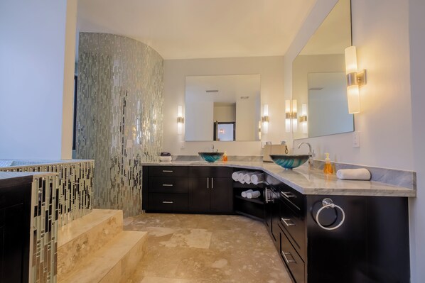 A modern bathroom with a curved vanity, a large mirror, and a glass bowl sink. - Diamante Beachfront Suites (San Pedro)