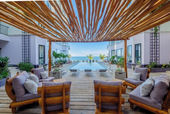 Terraza de madera con sillones de descanso y piscina, con vista al mar.