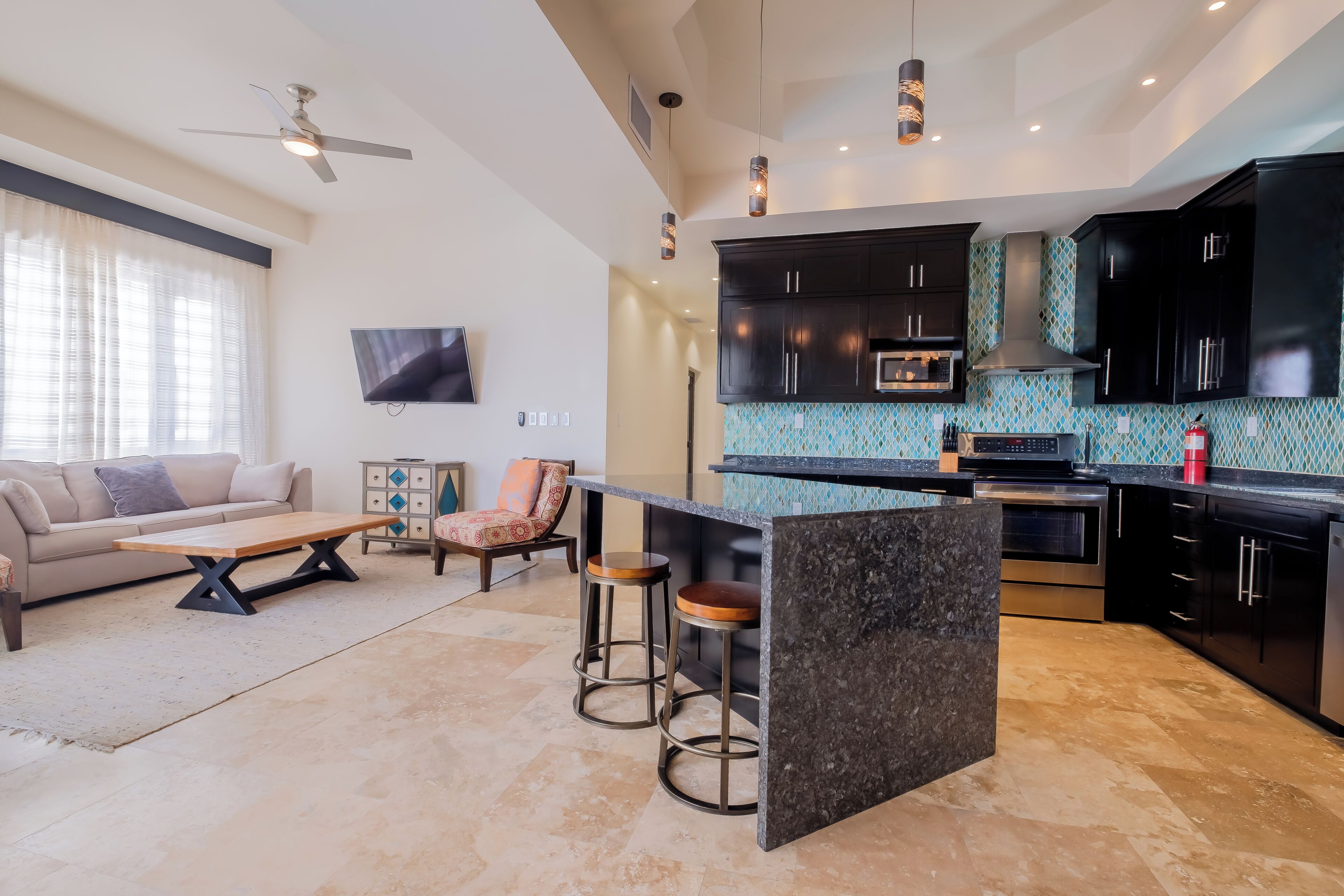 A modern kitchen with dark cabinets, a central island, and a dining area with a sofa and coffee table.