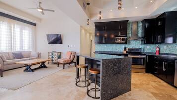 A modern kitchen with dark cabinets, a central island, and a dining area with a sofa and coffee table.