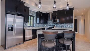 A modern kitchen with dark cabinetry, a stainless steel refrigerator, a granite countertop, and two bar stools.