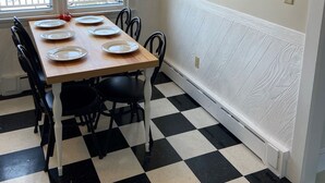 Un coin repas avec un sol à carreaux, une table en bois dressée avec des assiettes, des chaises noires et une grande décoration murale.