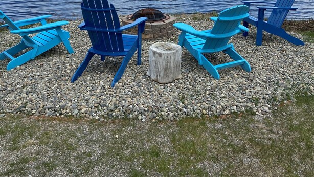 Une vue sur le lac, avec quatre chaises Adirondack bleues et un foyer installé sur une surface recouverte de gravier.