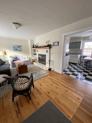 A living room with a fireplace, a checkered floor, and a kitchen area visible through an open doorway.