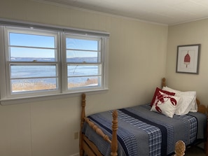 A bedroom with a bed, a window with a view of the sea, and a framed picture on the wall.