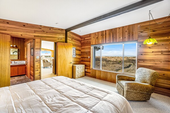 A bedroom with a large bed, a chair, and a window with a view.