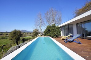 Ein Pool ohne erkennare Grenze mit Holzterrasse, zwei Liegestühlen und Blick auf eine gebirgige Landschaft.