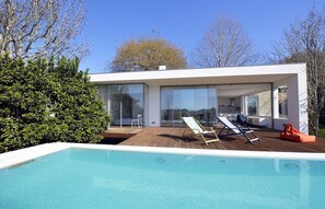 Una casa moderna amb piscina, grans finestres de vidre i terrassa de fusta.