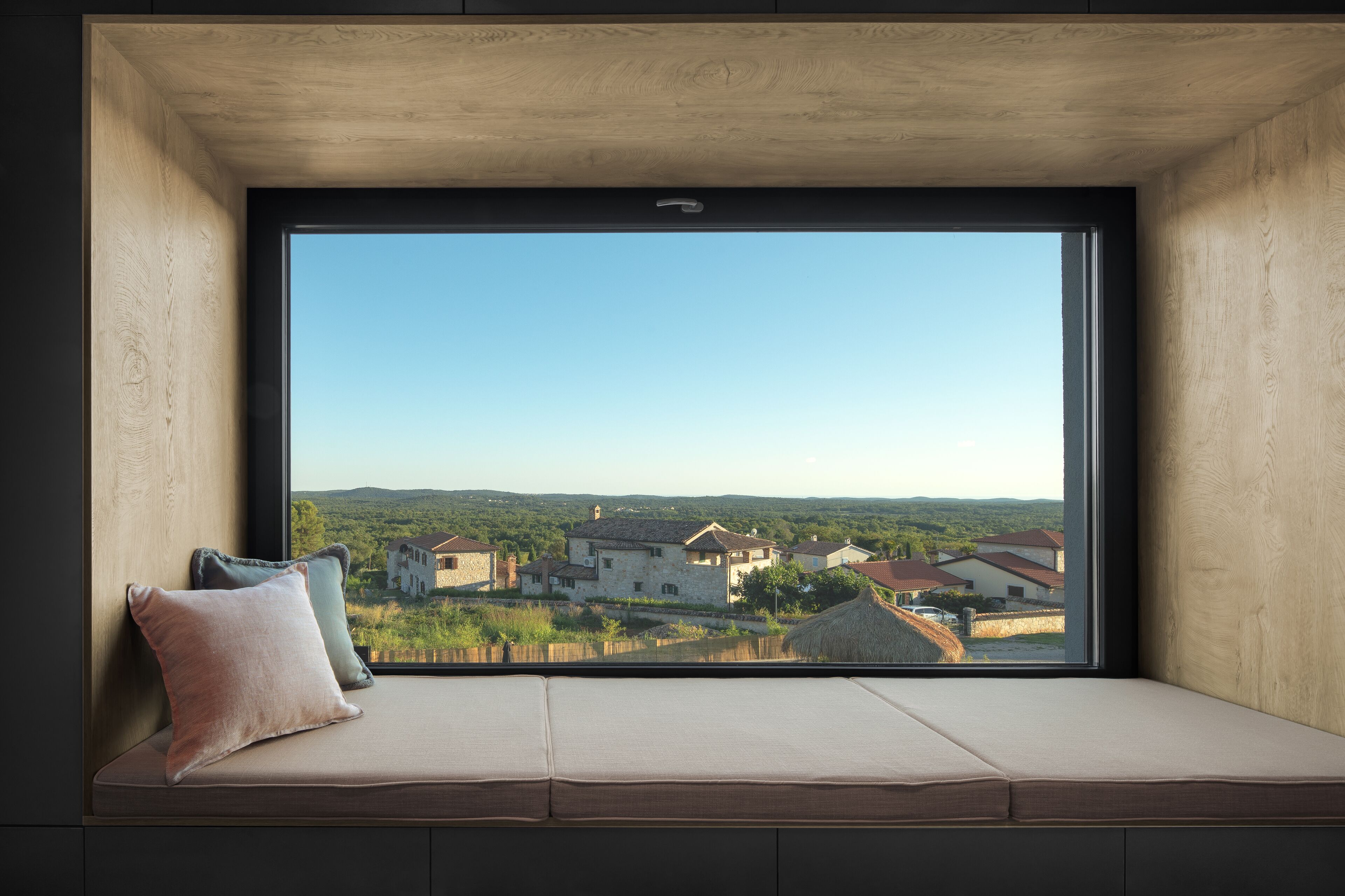 A window seat with cushions, a clear view of a rural landscape with houses and greenery.