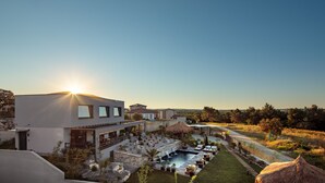 Eine moderne Villa mit Swimmingpool, Sitzgelegenheiten im Freien und einem strohgedeckten Gebäude.